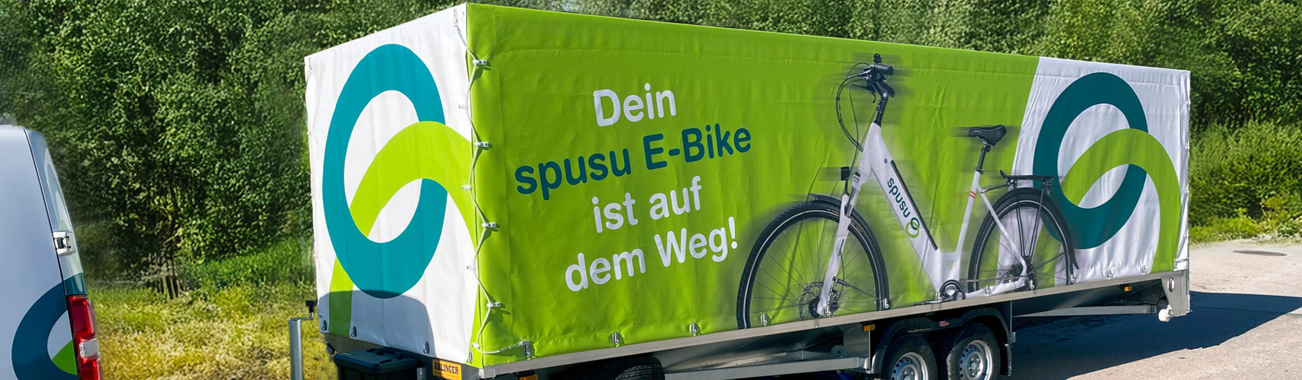 Individuell bedruckte Anhängerplane mit E-Bike-Werbemotiv auf einem Doppelachsanhänger.