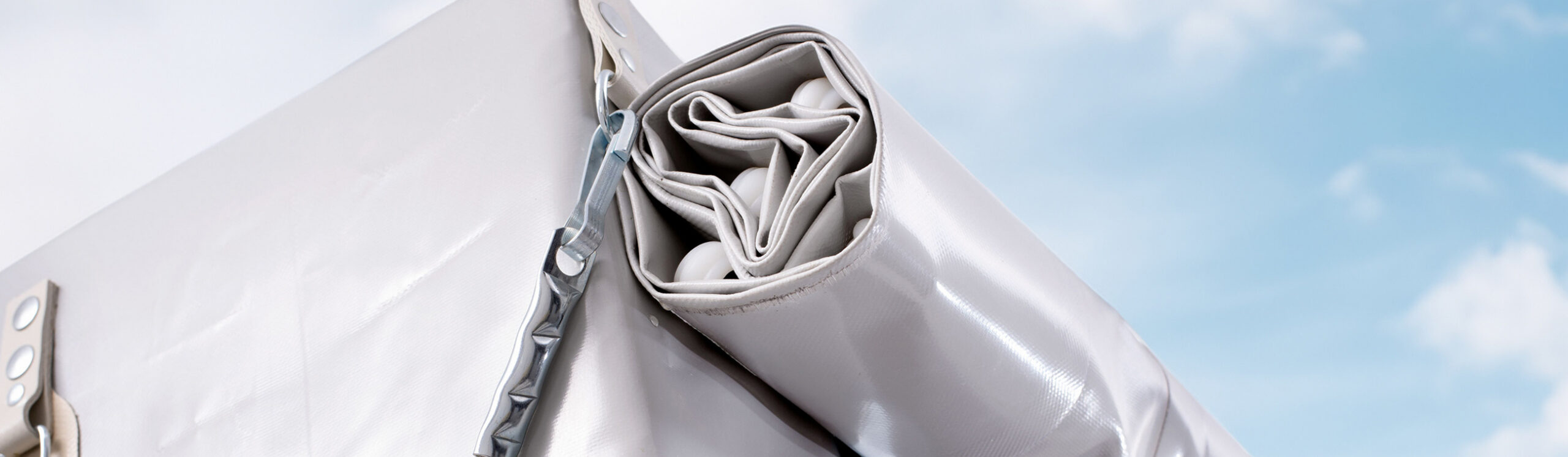 Detailaufnahme einer aufgerollten Plane mit Ösen und Spannverschluss am Anhänger.